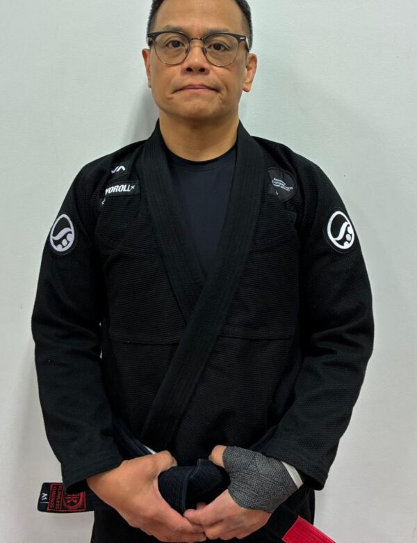 Professor Rico Maranan wearing a black Brazilian Jiu-Jitsu gi and holding his black belt.