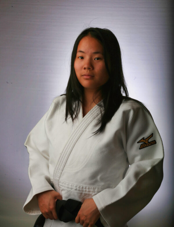 Sensei Rhiannon Lau wearing a white Judo gi and black belt for her coaching profile.