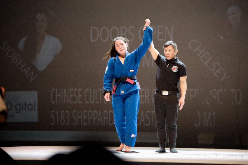 Professor Shiv Barnes having her arm raised after winning a Brazilian Jiu-Jitsu superfight.