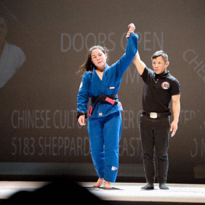 Professor Shiv Barnes having her arm raised after winning a Brazilian Jiu-Jitsu superfight.