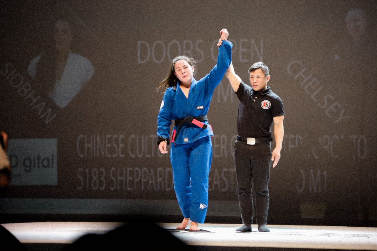 Professor Shiv Barnes having her arm raised after winning a Brazilian Jiu-Jitsu superfight.