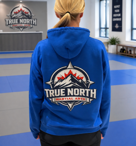 Back view of a blue hoodie displaying the large True North Martial Arts logo inside the Newmarket academy.